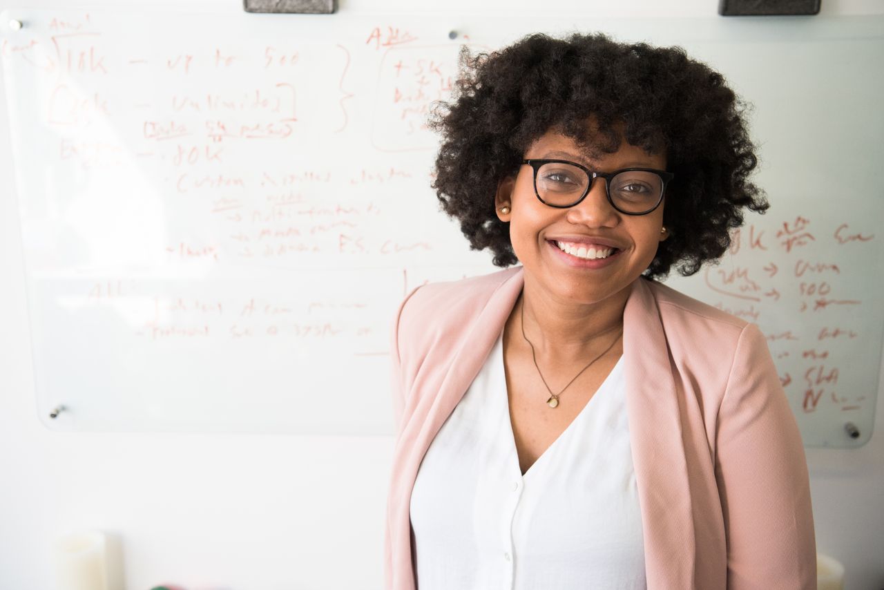 social-feed-img-02 Smiling businesswoman with glasses and afro hairstyle in an office setting.