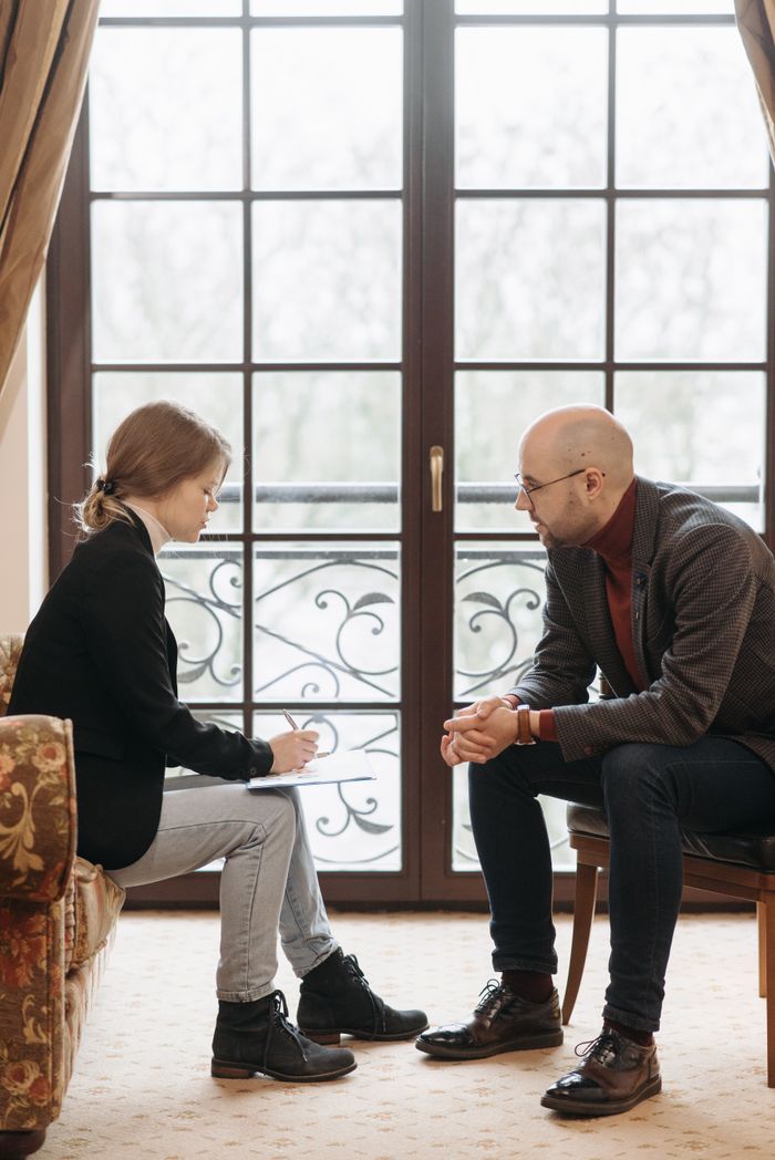 quality-assurance-02 Two adults sitting by a window engaged in a professional conversation.